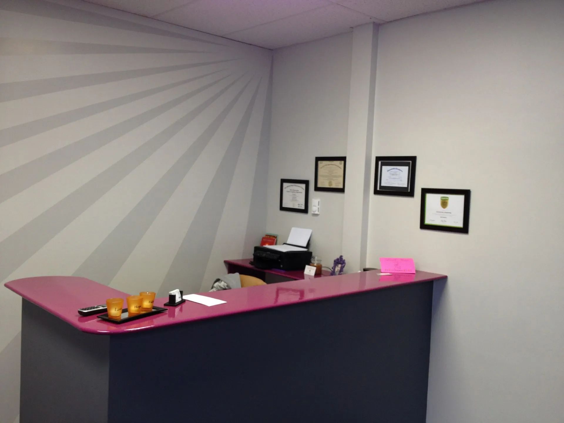 Reception area with pink and gray desk, gray walls, and diplomas.