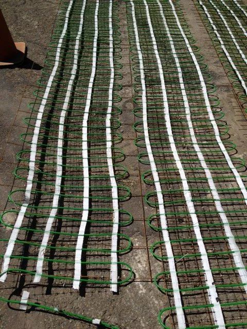 Green and white radiant heating mats laid out on a concrete surface, ready for installation.