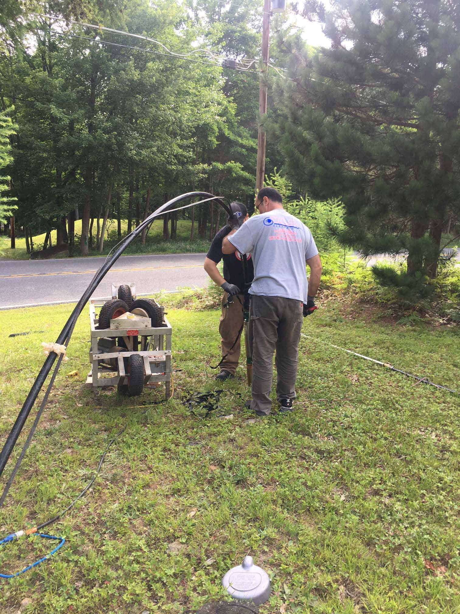 Two men by well, working on equipment with water spraying; outdoors.