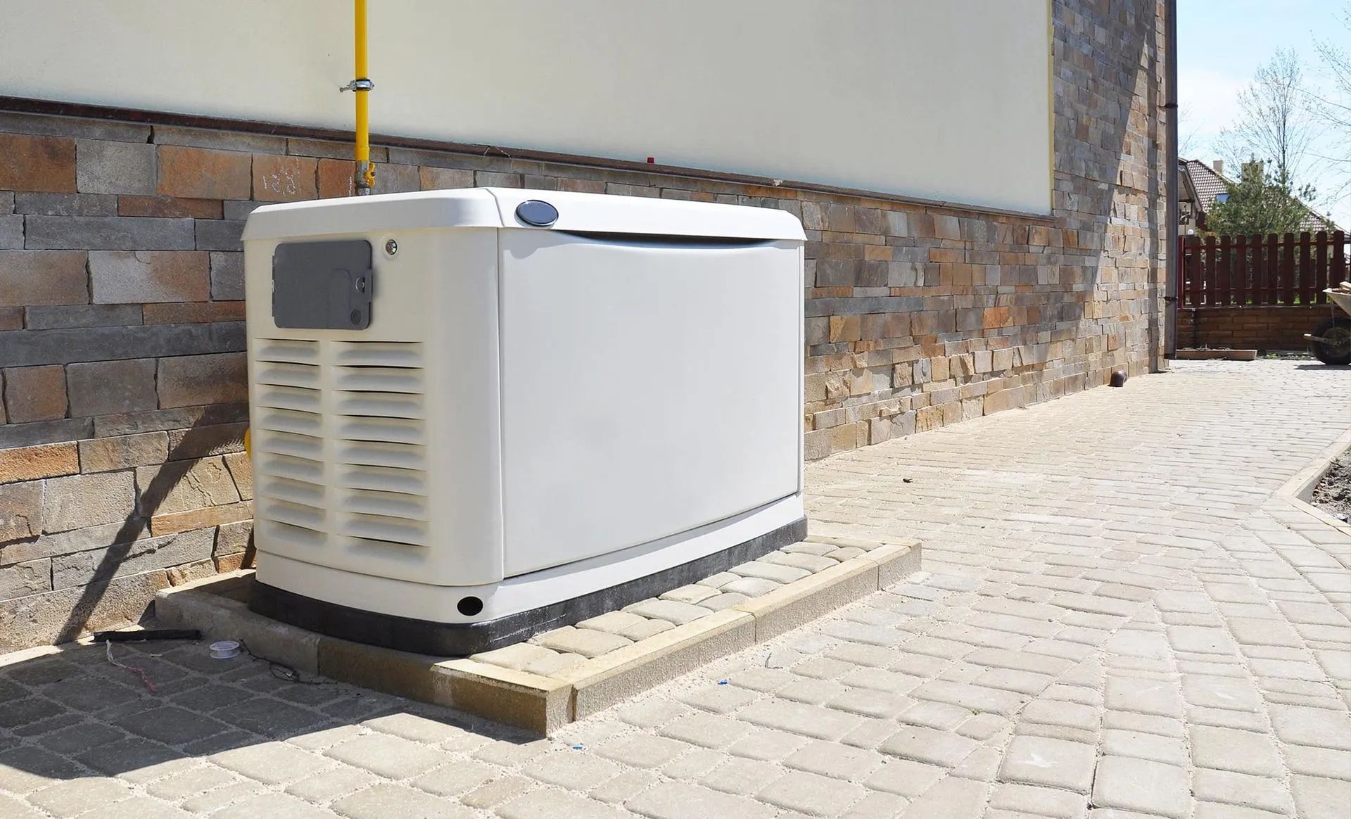 A standby generator outside a building. It's white and sits on a concrete pad next to a brick wall.
