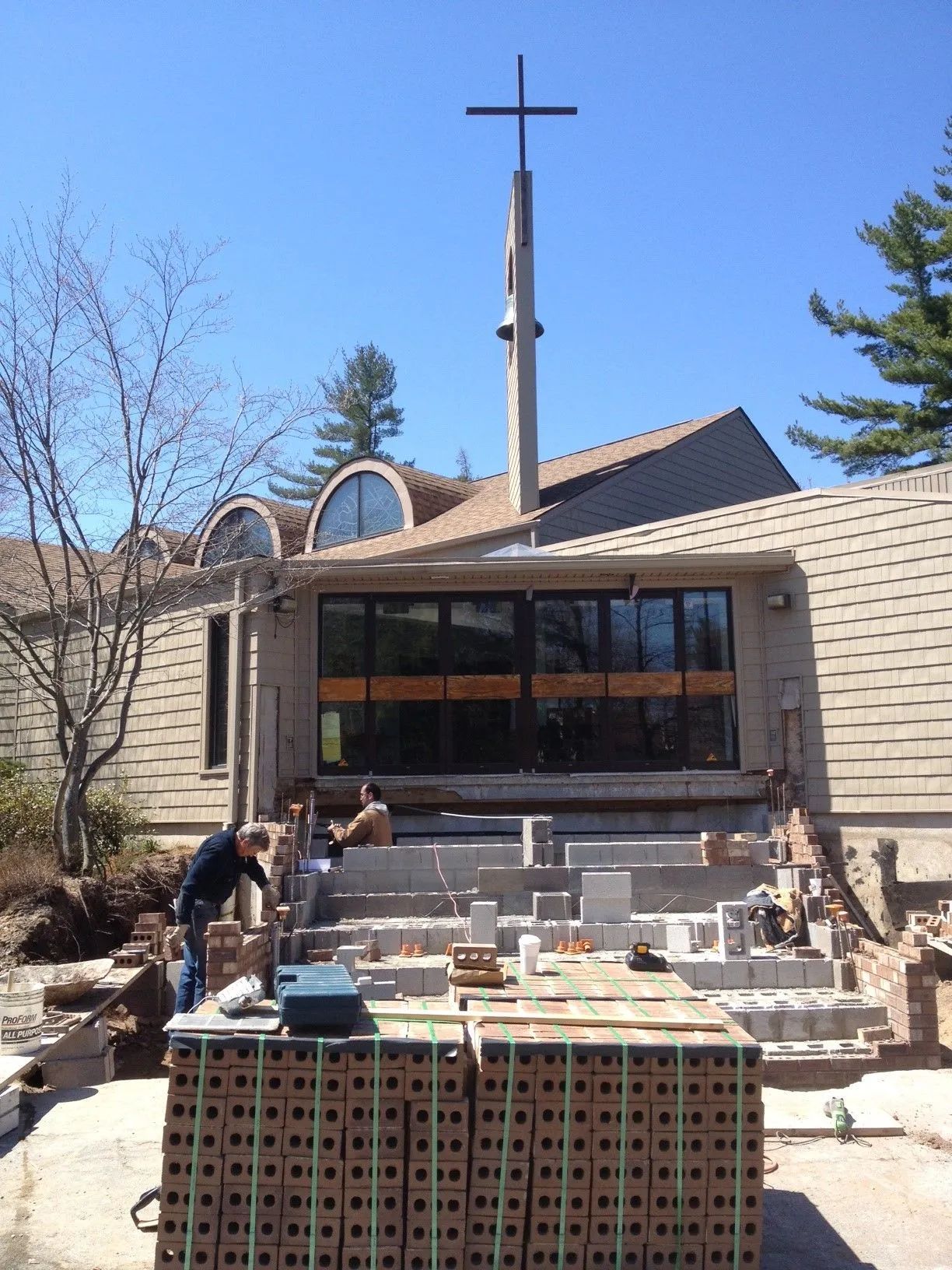 Church under construction with workers, bricks, and a cross.