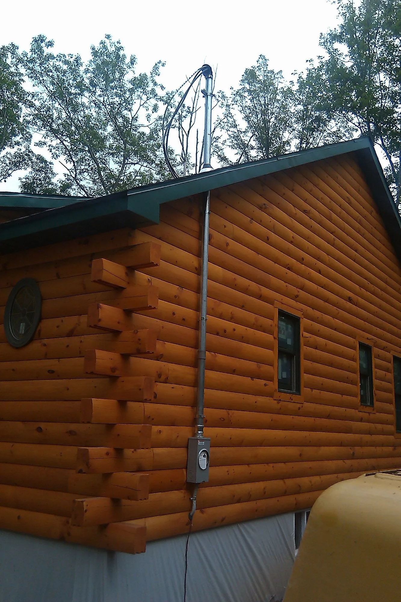 Wooden log cabin with metal electrical conduit running up the side to the roof.