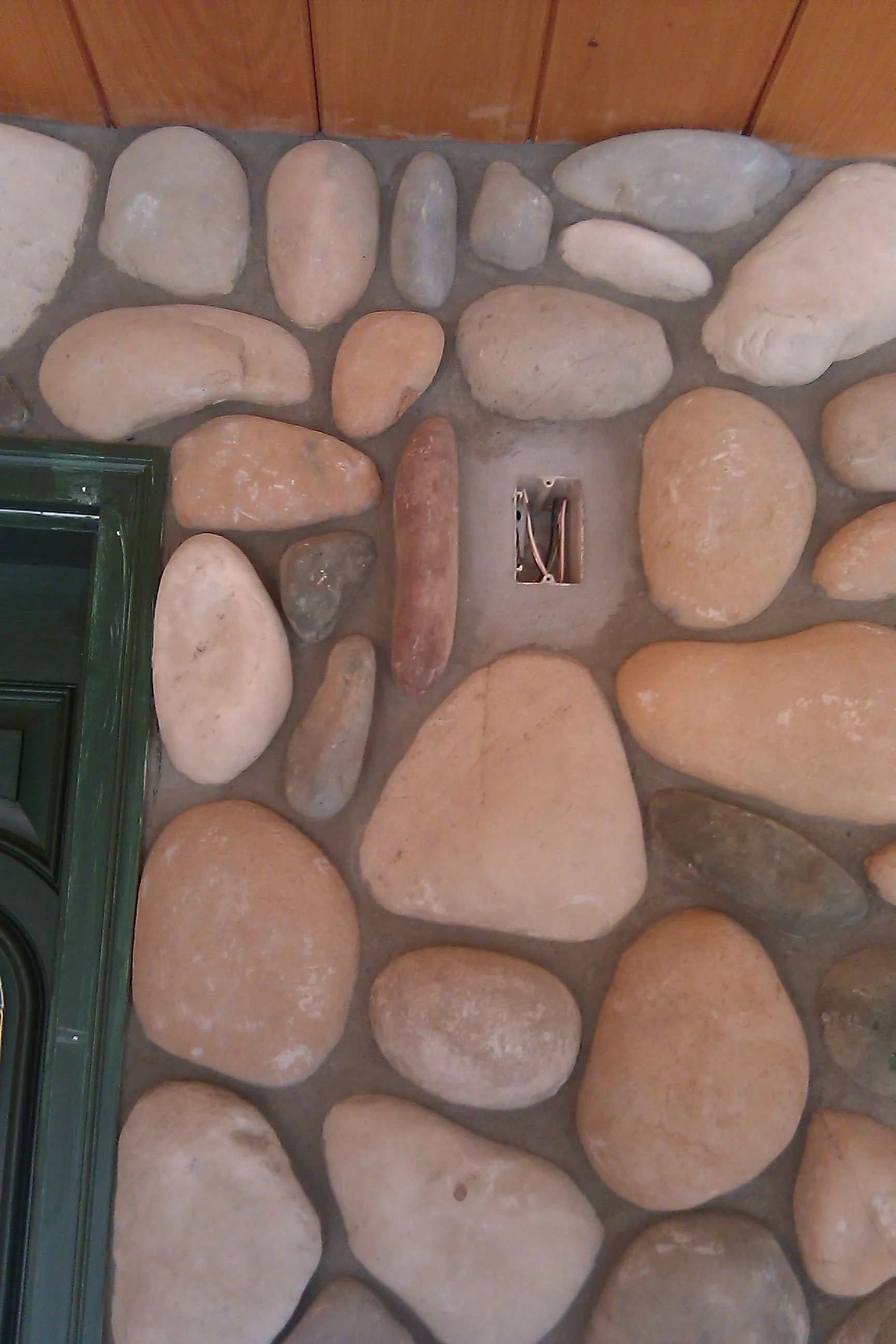 Stone wall with embedded electrical outlet, next to a green door frame.