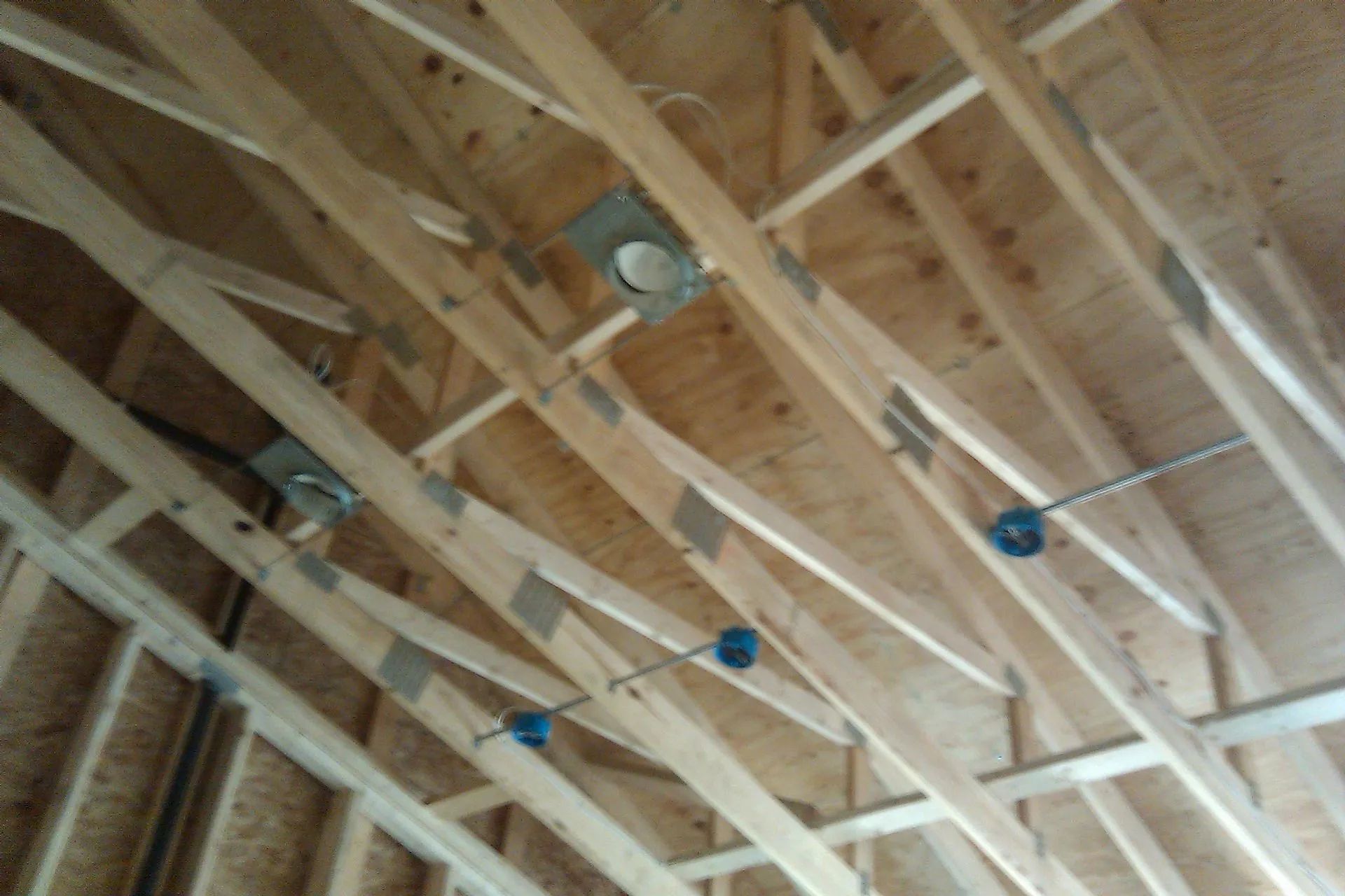 Wooden rafters with recessed lighting fixtures and electrical boxes in a new construction.