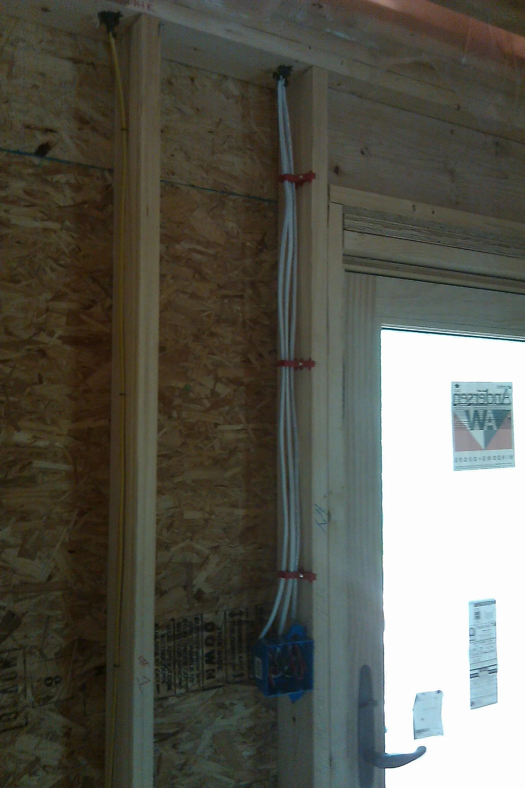 Electrical wiring in a wood-framed wall, secured with red clips. A blue electrical box is visible.