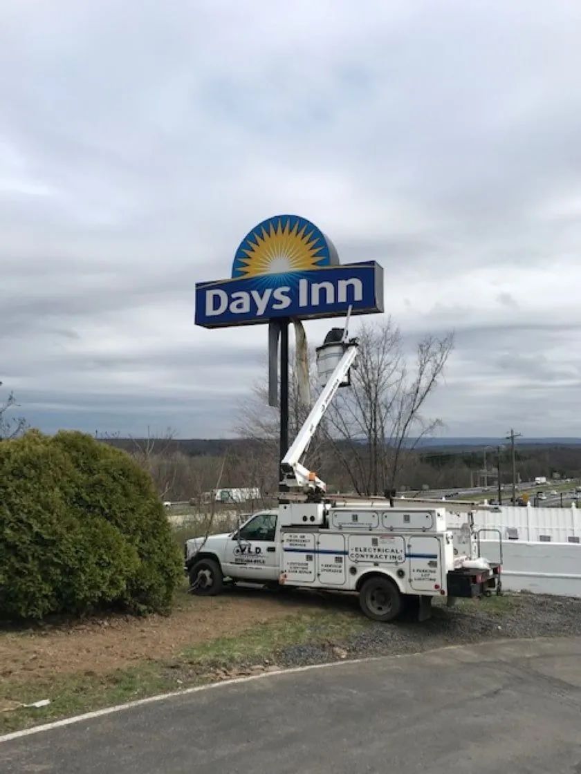 A service truck with a boom lift working on a Days Inn sign under a cloudy sky.