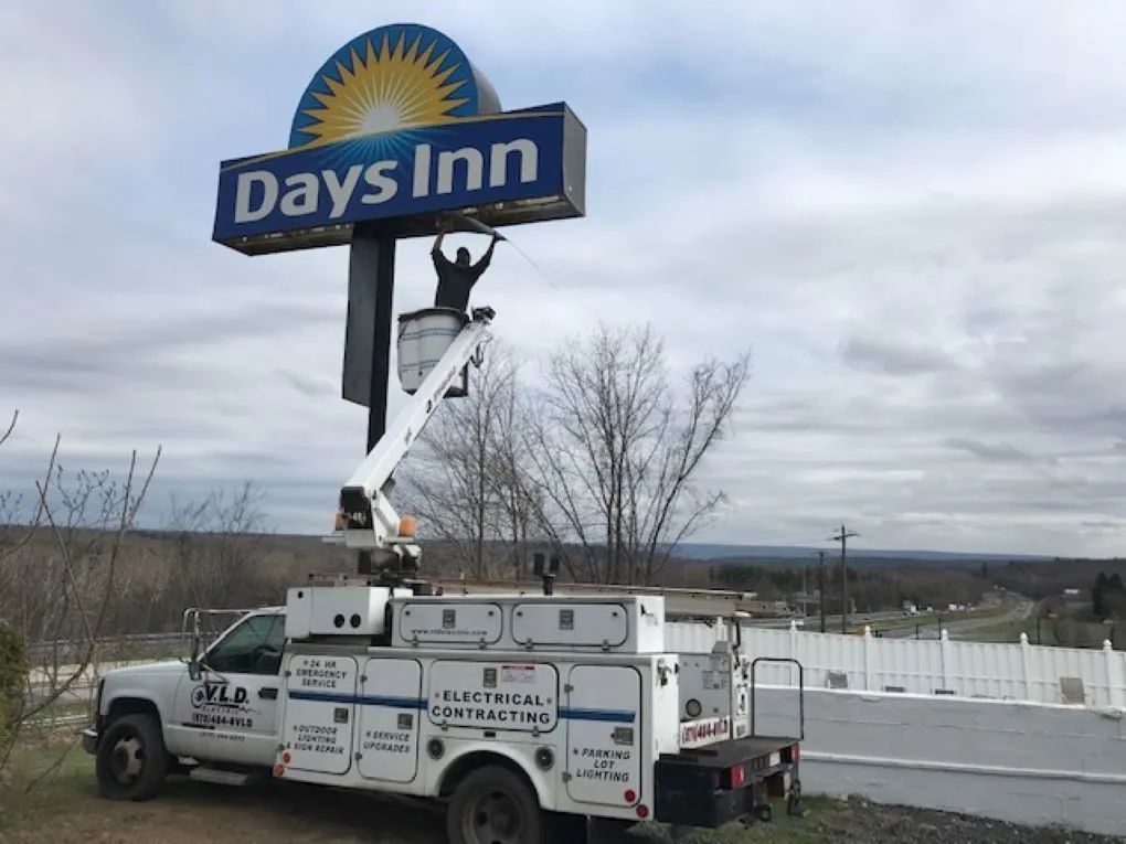 Electrician in a lift truck repairing a Days Inn sign outdoors, cloudy sky.