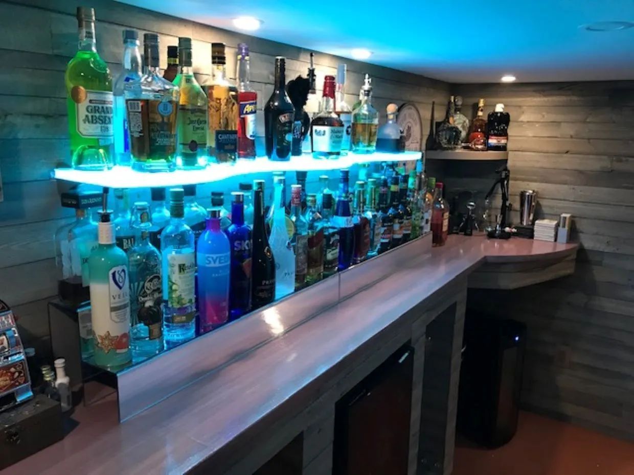 Bar with bottles of liquor on lit shelves, wood paneling, and a pink countertop.