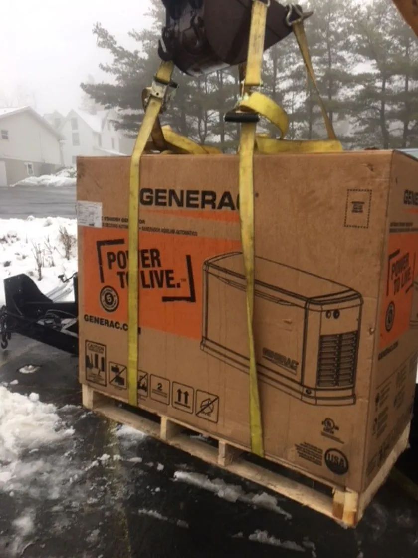 Generator on a pallet being lifted by straps, on a trailer with snowy ground and trees in background.