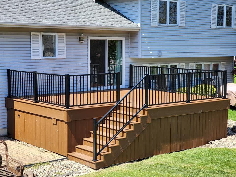 A wooden deck with stairs and a black railing in front of a house.