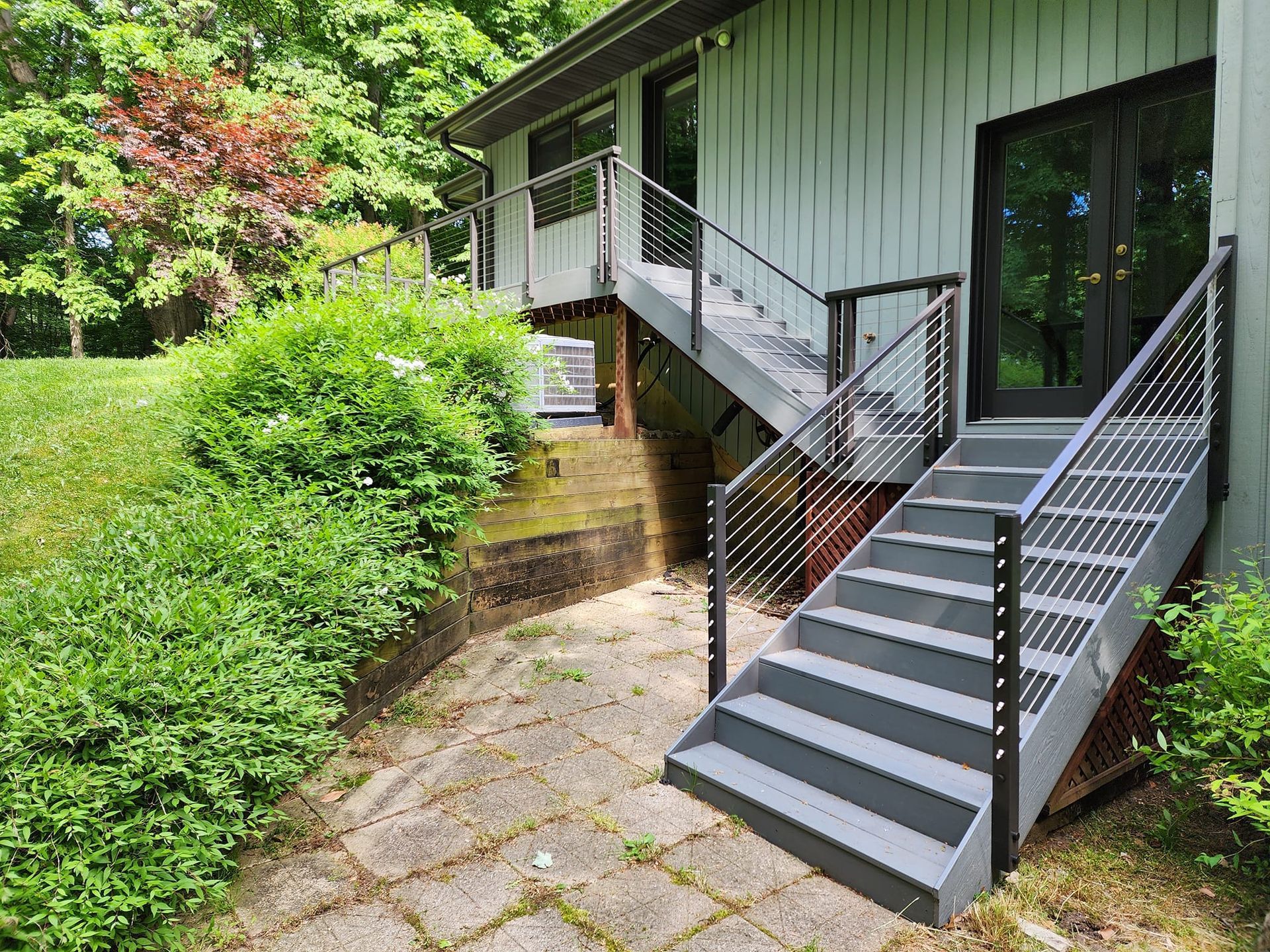 A house with stairs leading up to a deck and a patio.