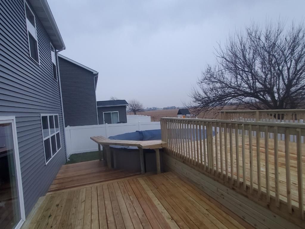 A wooden deck with a bench and a fence in front of a house.