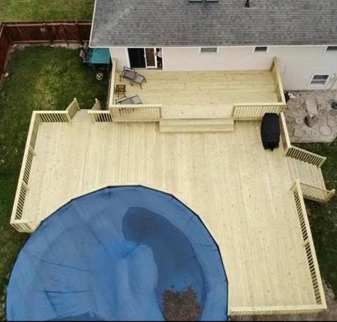 An aerial view of a wooden deck with a pool and a house in the background.