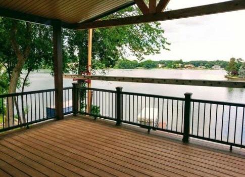 A wooden deck with a black railing overlooking a lake.