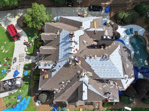 An aerial view of a residential roof undergoing repair, featuring workers, construction materials, and a backyard pool.