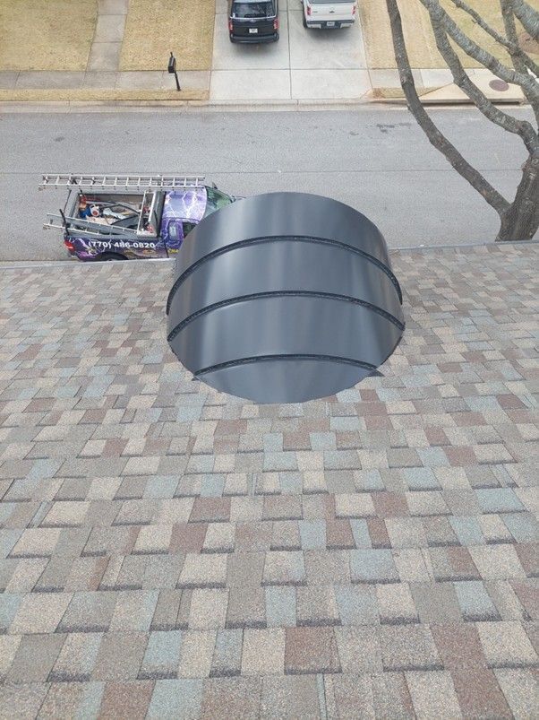 A metal, arched roof vent installed on a shingled roof, with a street, parked vehicles, and a utility truck visible below.
