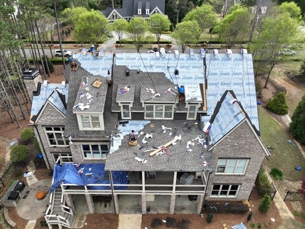 Aerial view of a multi-story brick home under construction with workers installing new roofing materials.