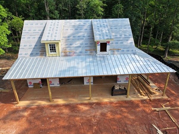 An elevated view of a house under construction, featuring a metal roof, two dormer windows, and a large front porch.