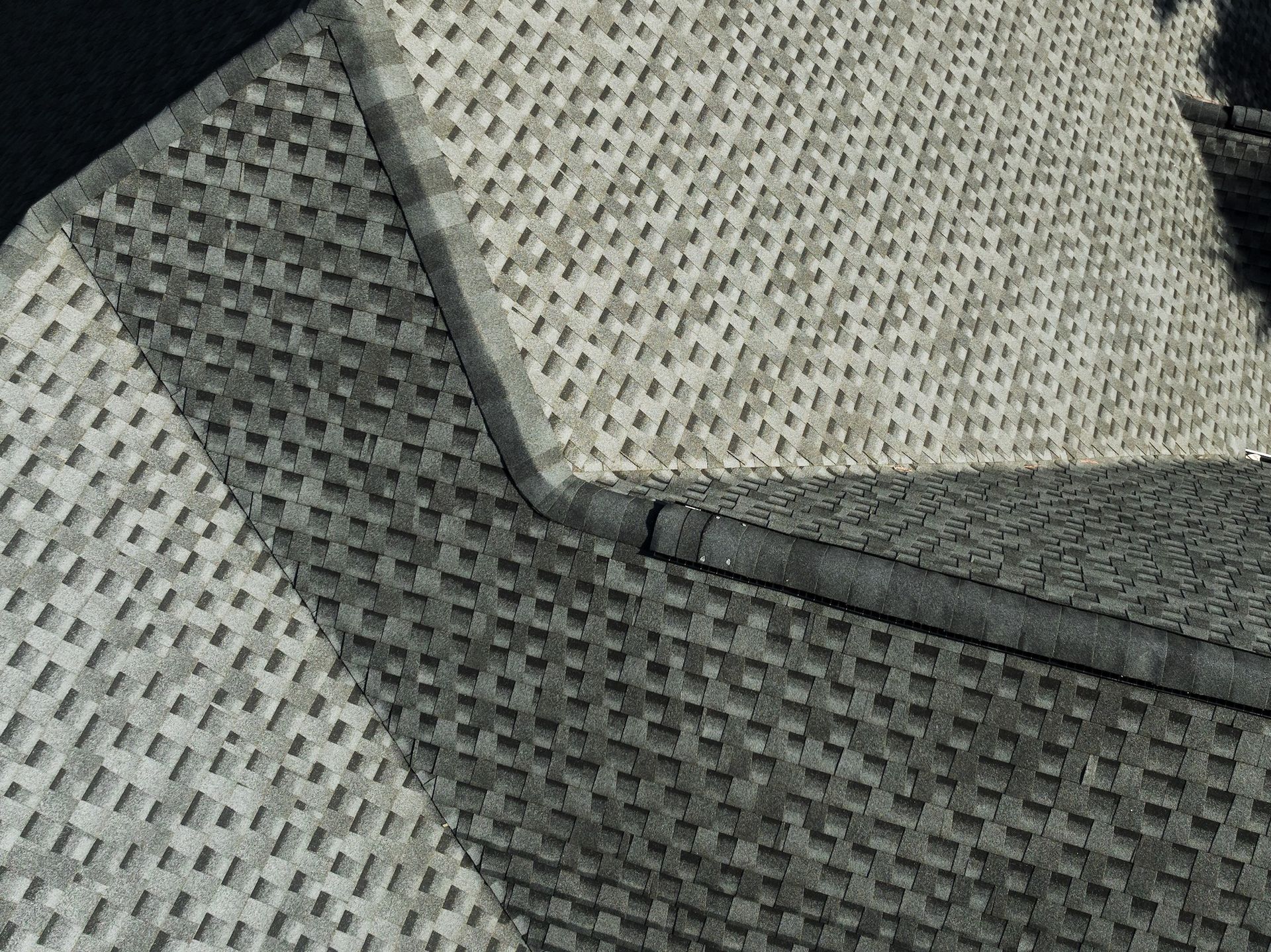 Overhead view of a gray shingled roof with shadows and angled planes.