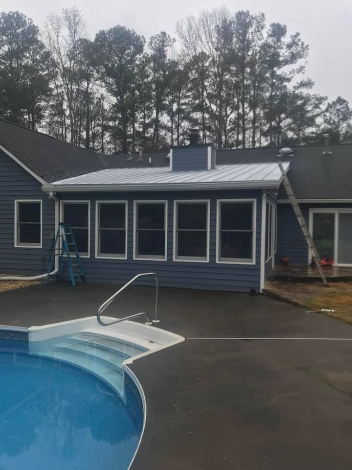 Blue house with a screened porch and pool in the foreground, overcast sky.
