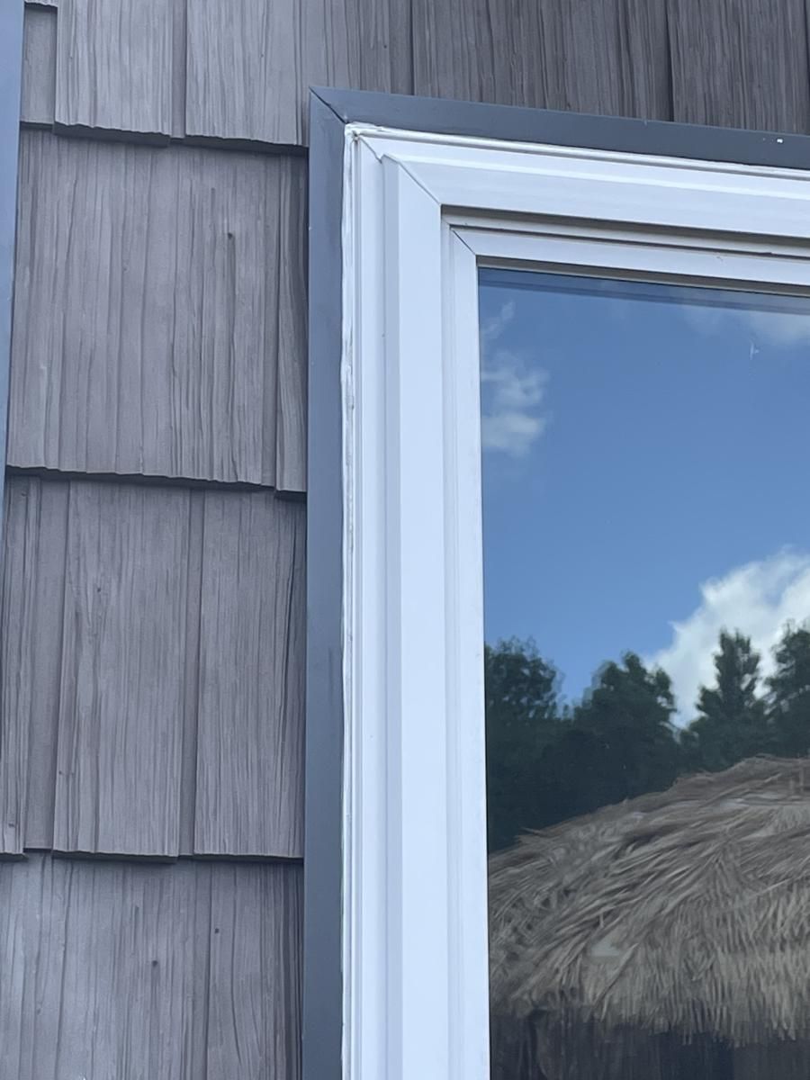 Corner of a gray wooden-shingled wall and a white window frame with a dark gray trim.