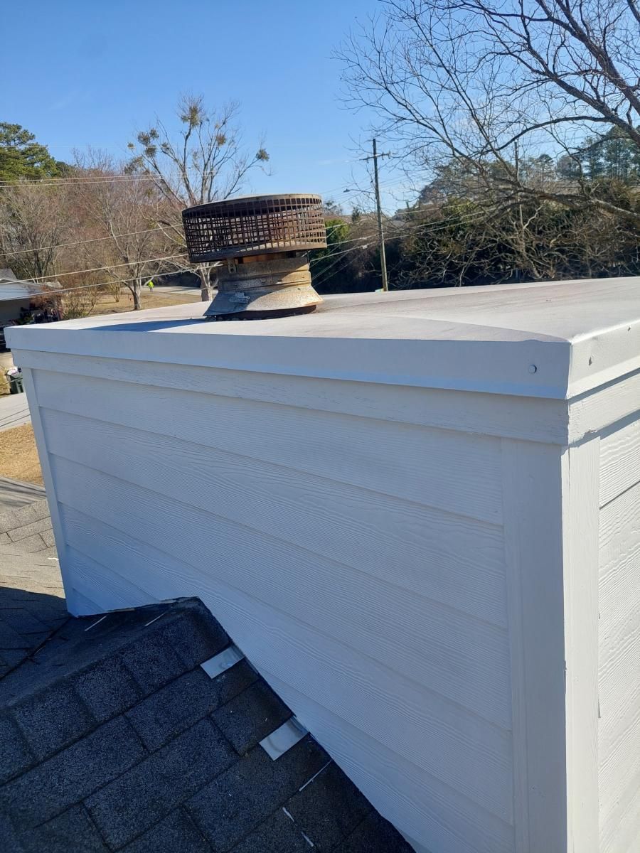 Chimney on a white, flat-roofed building. Brown chimney cap; white siding and trim.