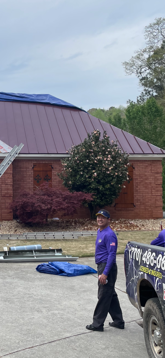A worker walks toward a house with a damaged roof, next to a truck.