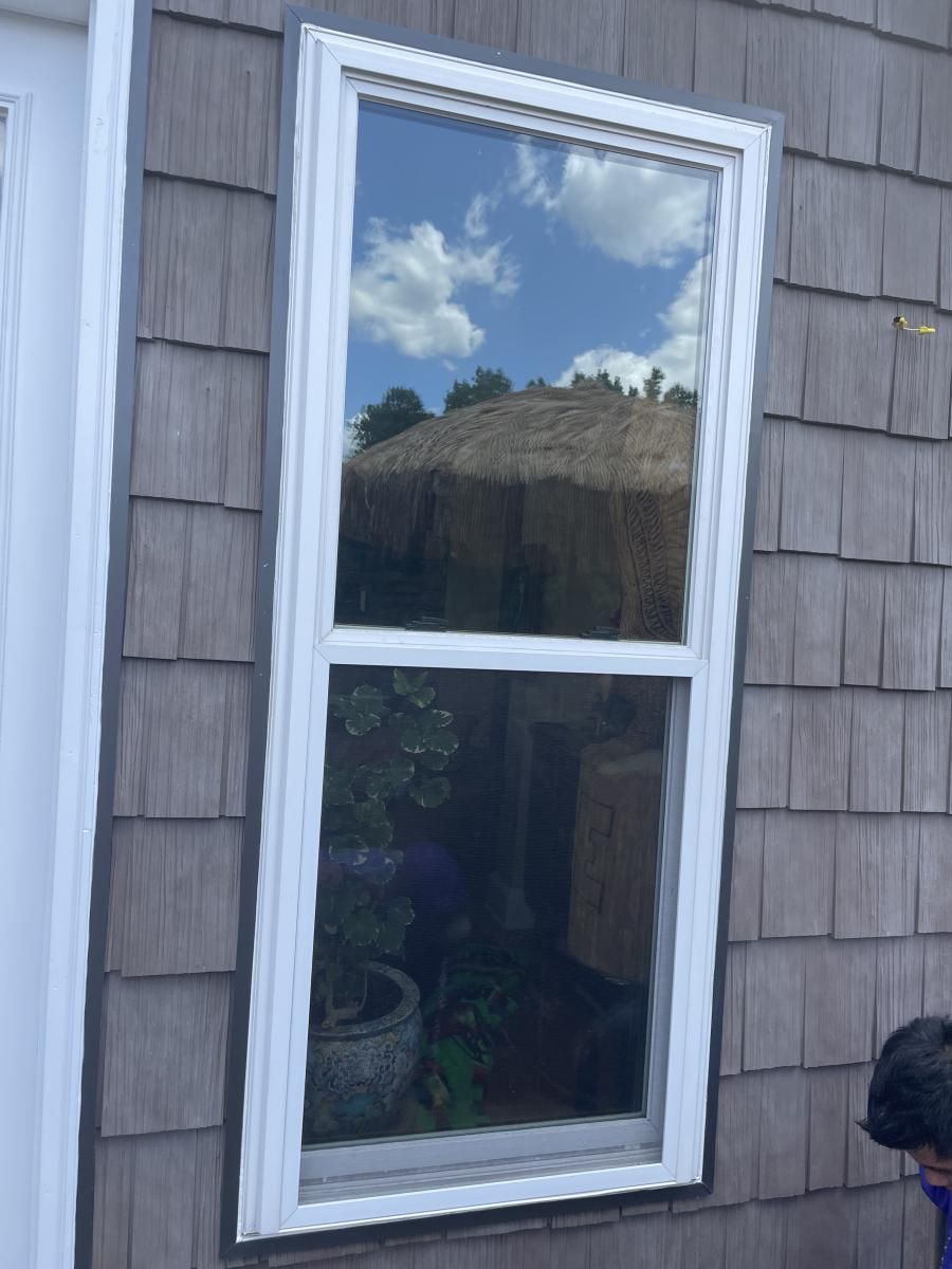 White-framed window reflecting blue sky and clouds, set in a gray shingled wall.