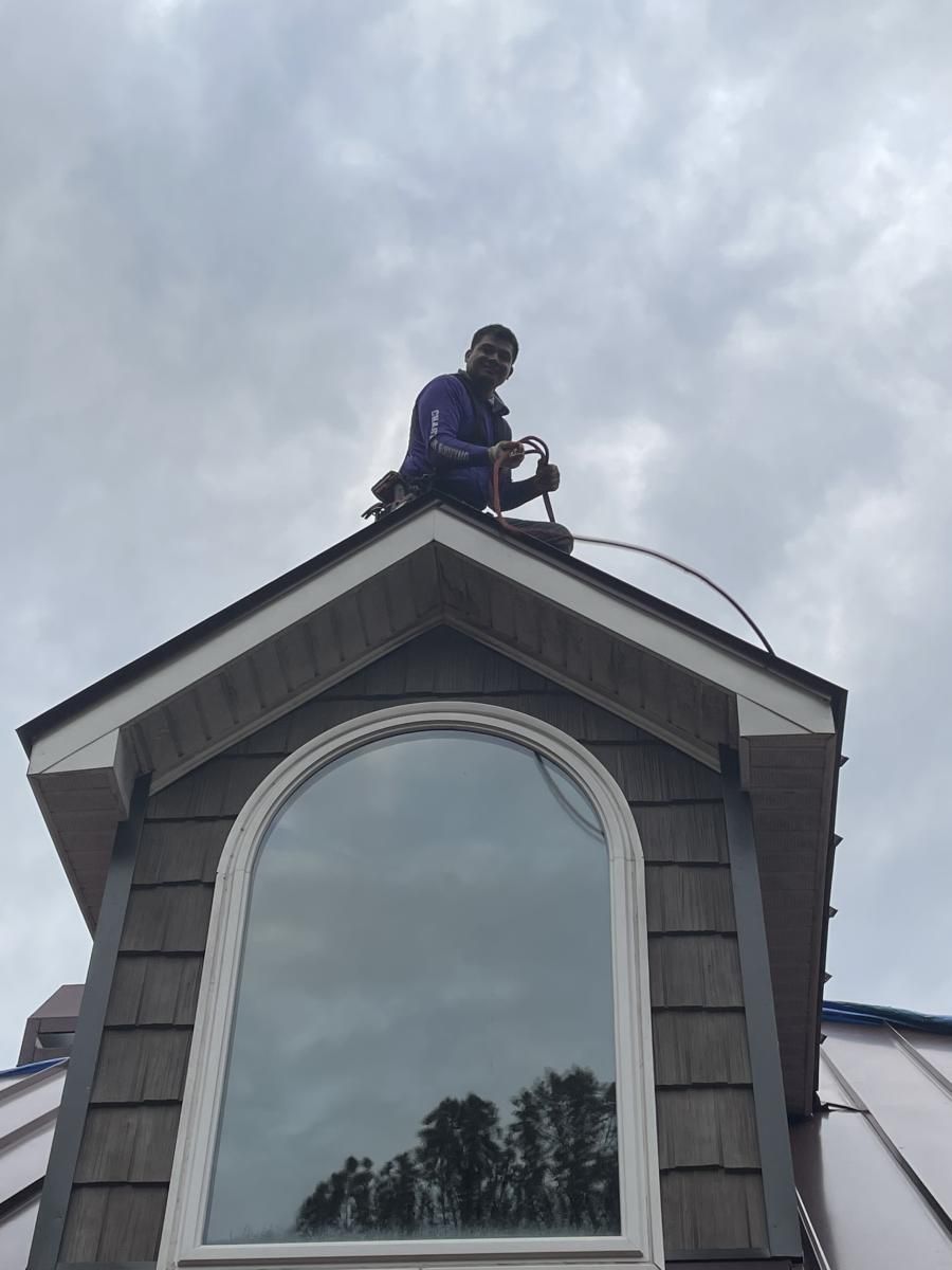 Man on roof, cloudy sky. He's installing or repairing metal. Window below.