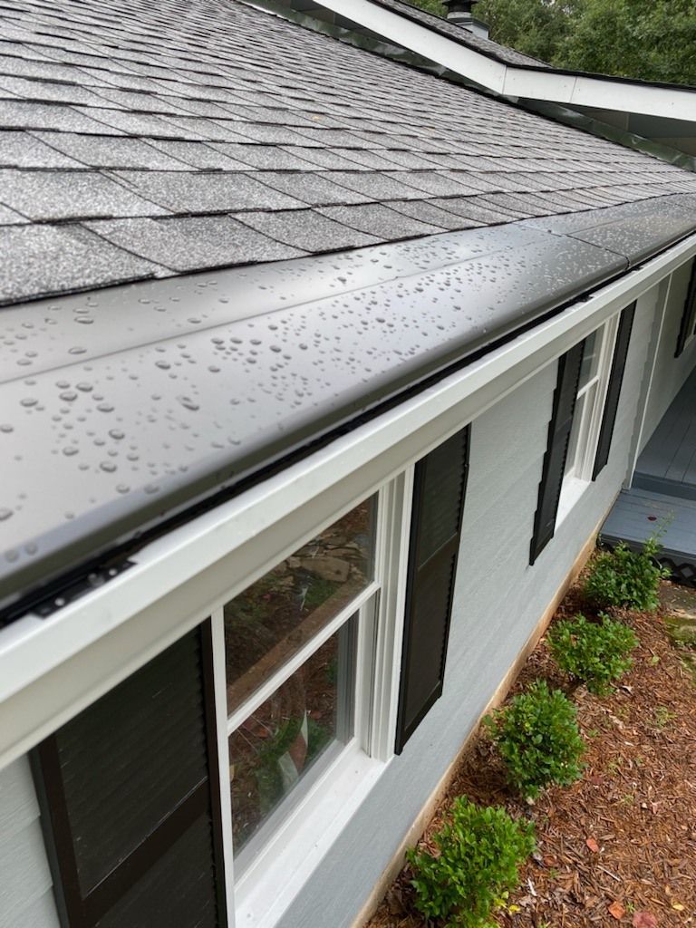 Gray house exterior with black roof and gutter, rain droplets, white window frames, and dark shutters.