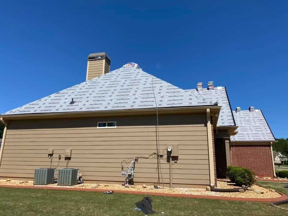 House with new roofing material, tan siding, and a clear blue sky.