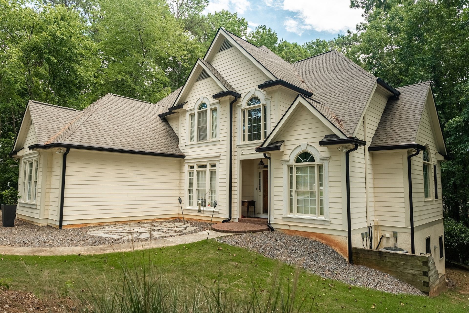 Beige house with dark trim, surrounded by green lawn and trees.