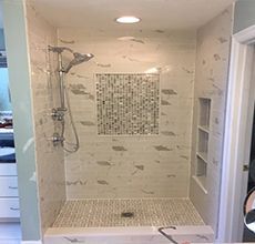 A bathroom with a walk in shower and a mosaic tile wall.
