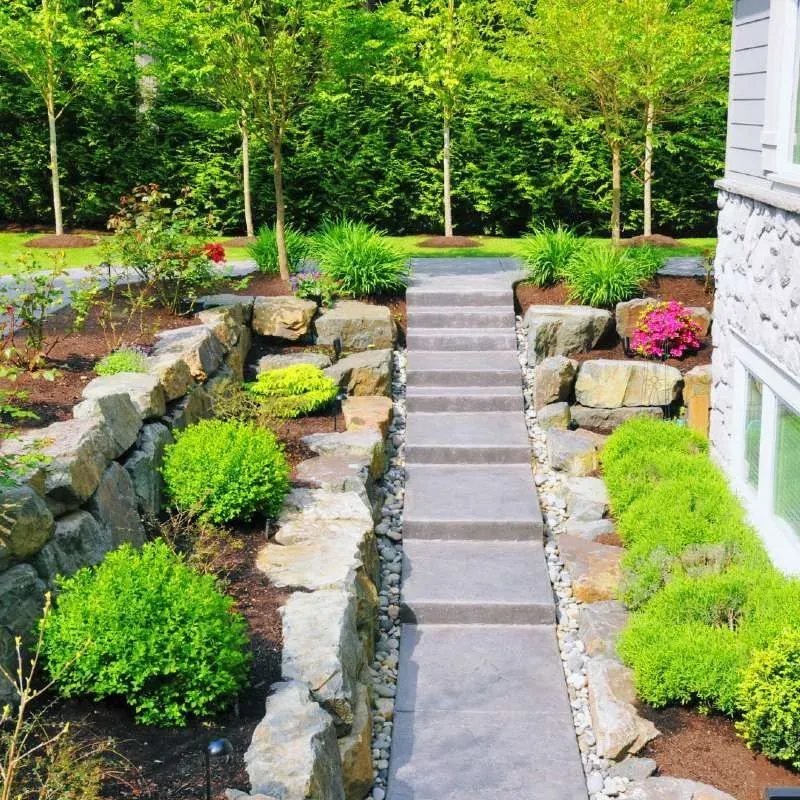 Stone staircase with tiered landscaping, lush greenery, and retaining walls.