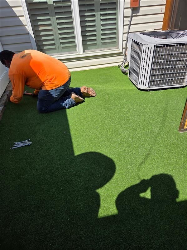 Person installing artificial turf on a patio next to a window and an air conditioner.