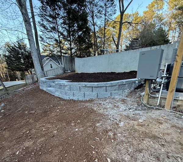Stone retaining wall with steps, mulch bed, and a concrete wall in a yard.