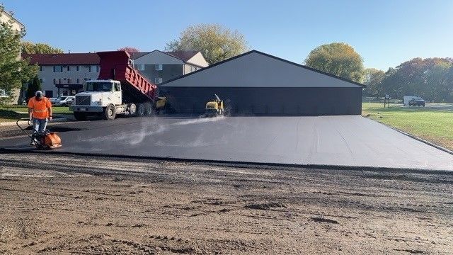 A dump truck is being loaded with asphalt in front of a garage.