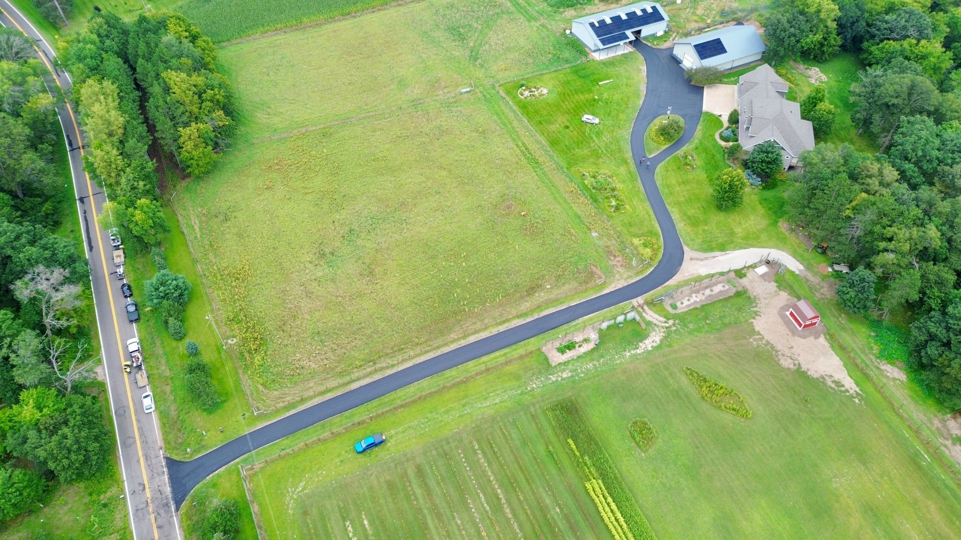 An aerial view of a road going through a lush green field.