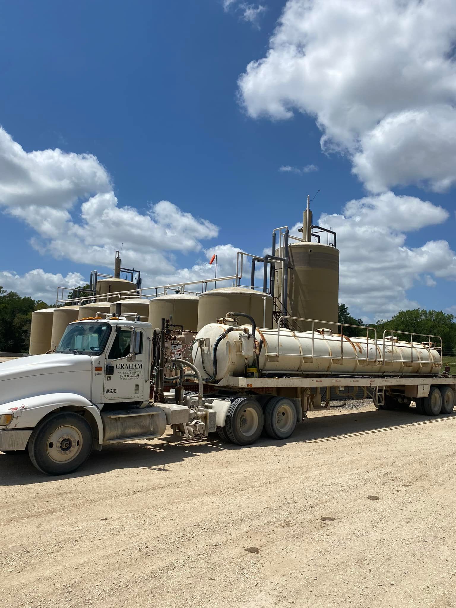 A white truck is parked in a dirt lot next to a large tank.