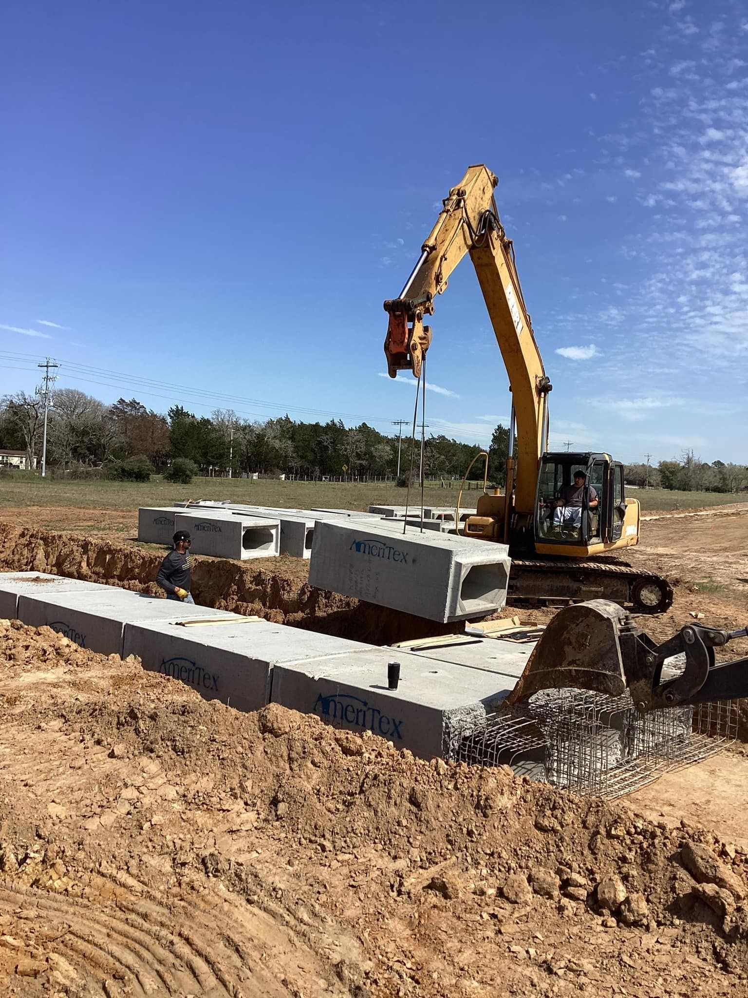 A large yellow excavator is moving concrete blocks in a dirt field.
