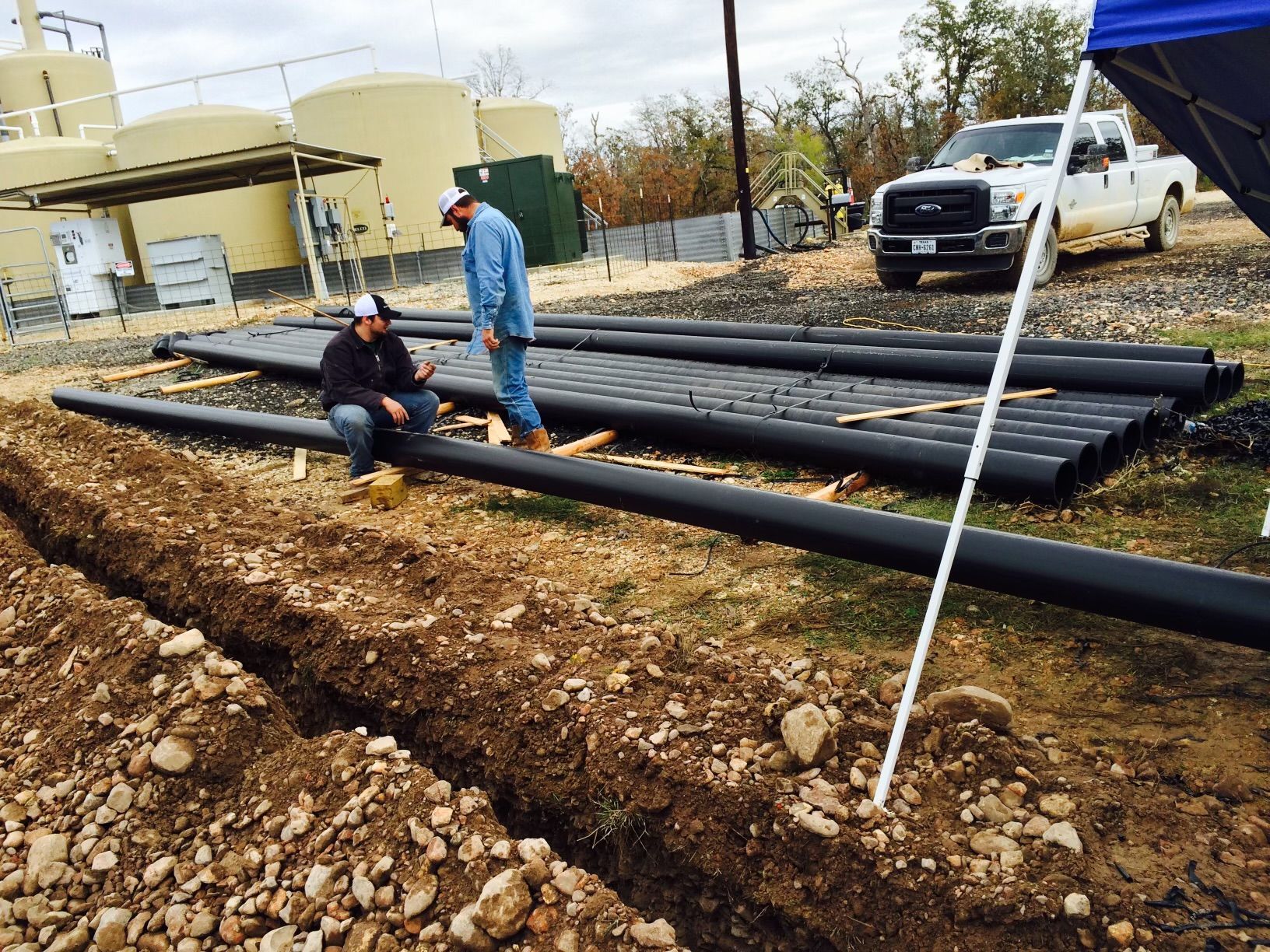 Two men are working on a pile of pipes in the dirt