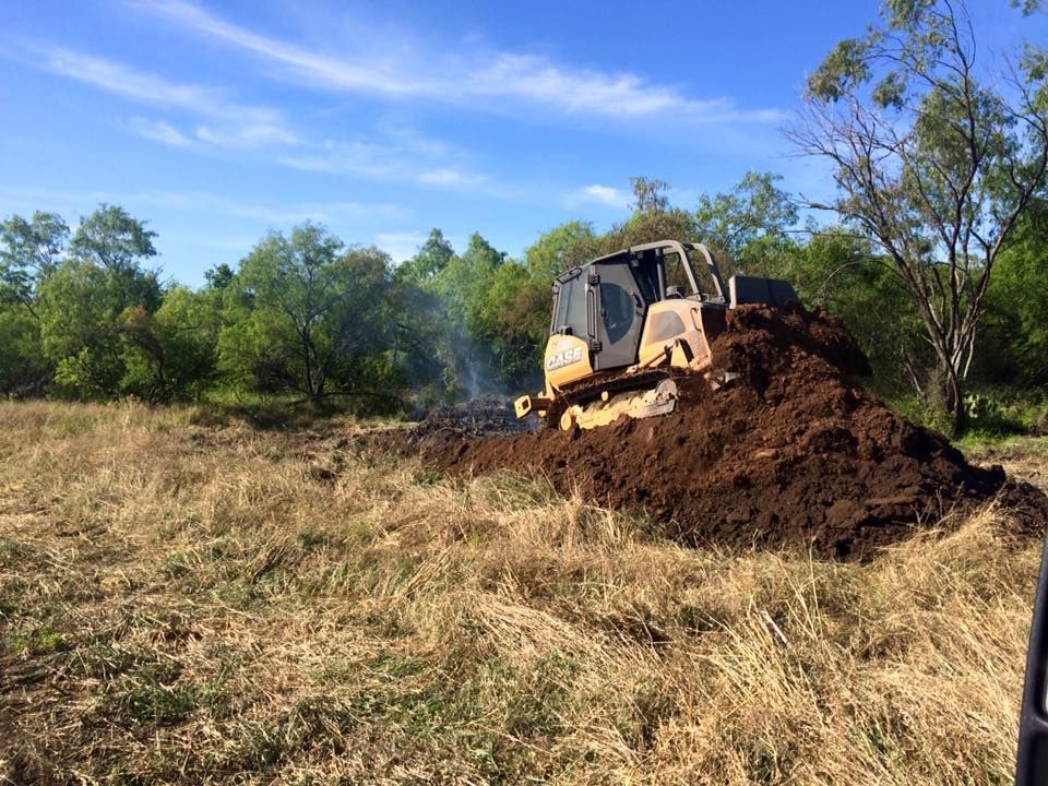 A bulldozer is moving a pile of dirt in a field.