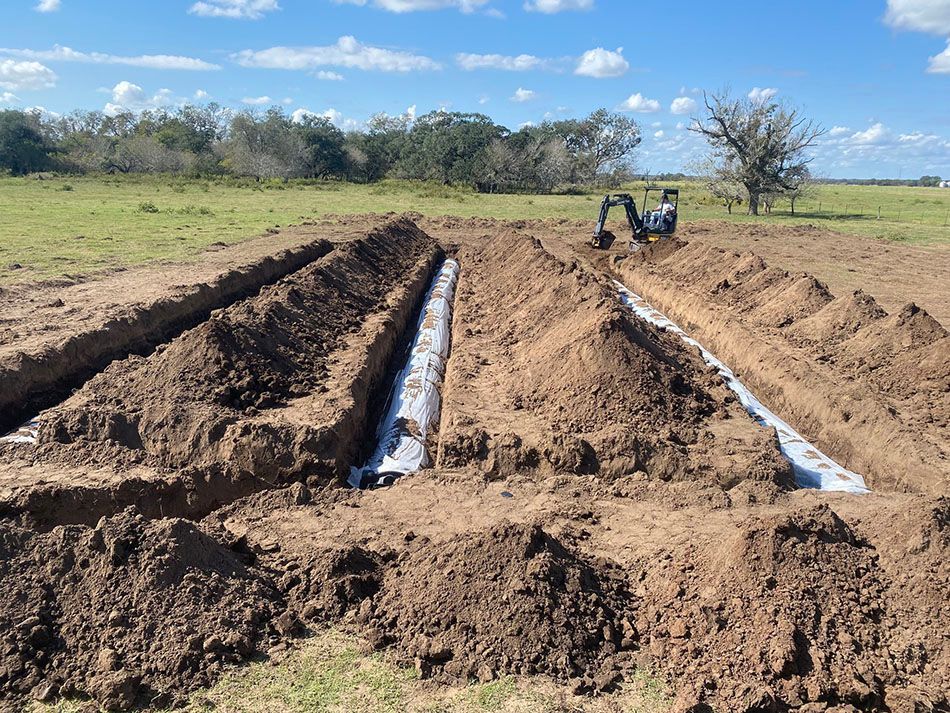An excavator is digging a trench in the dirt in a field.