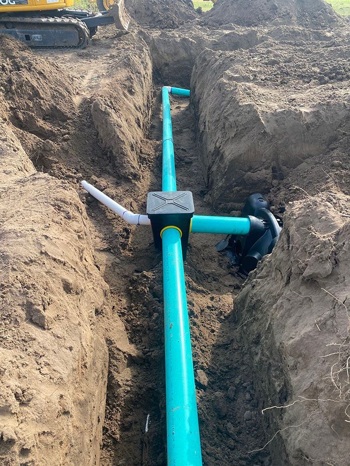 A green pipe is being installed in a trench in the dirt.