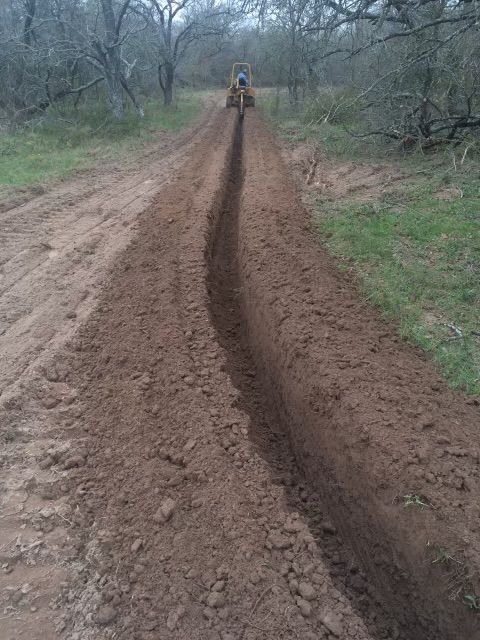 A tractor is digging a trench in the dirt on a dirt road.