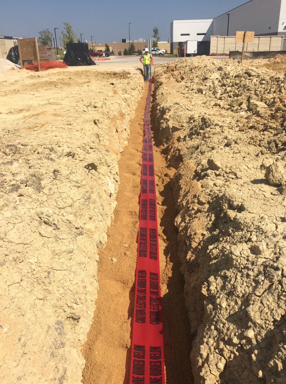 A man is standing in a trench with a red tape that says do not enter.