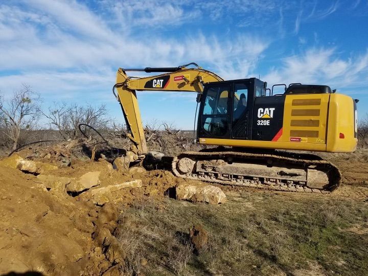 A yellow cat excavator is digging a hole in the dirt.