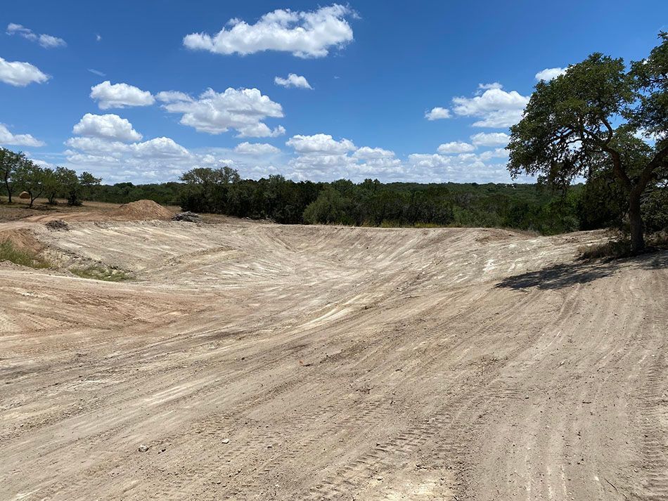 A dirt road with trees in the background and a blue sky with clouds.