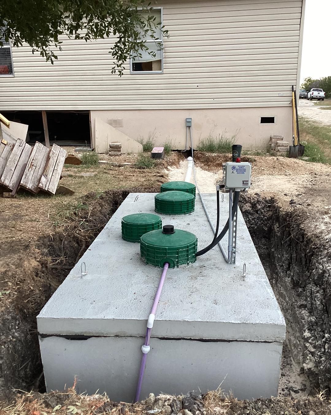 A septic tank is sitting in the dirt in front of a house.