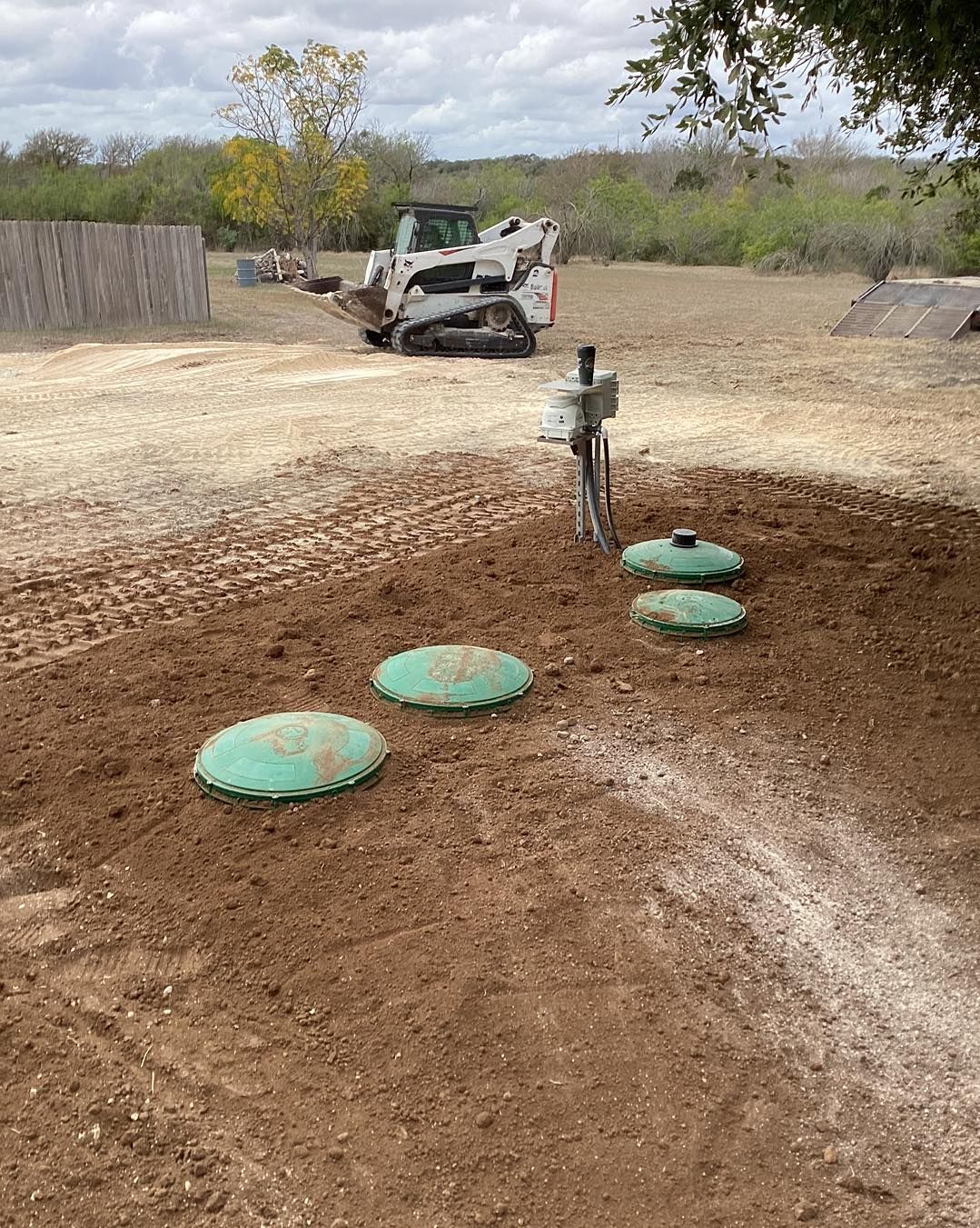 A bulldozer is working on a septic system in a dirt field.